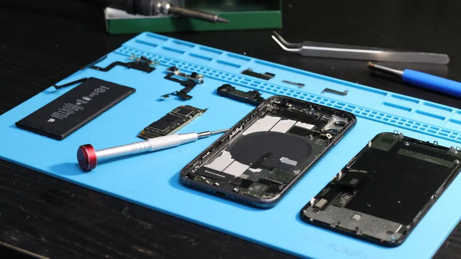 En adskilt smartphone med batteri, skruetrækker og pincet på en blå reparationsmåtte
