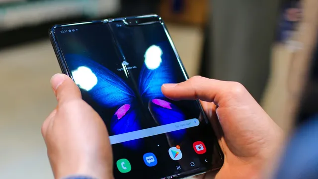 To hænder holder en udfoldet foldbar smartphone med en blå sommerfugl på skærmen