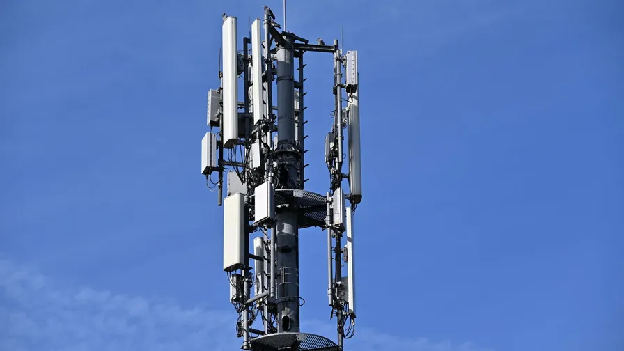 Mobilmast med mange hvide antenner mod en klar blå himmel
